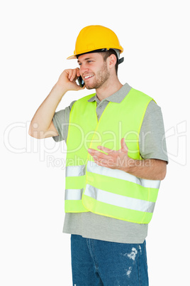 Smiling young construction worker discussing on the cellphone