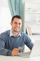 Smiling male with credit card at his notebook
