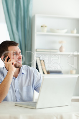 Smiling businessman in his homeoffice using his cellphone