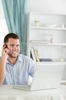 Smiling businessman in his homeoffice on the phone