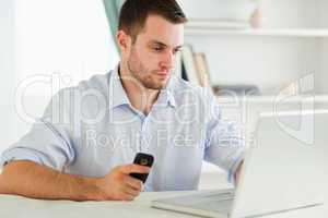 Businessman typing on his laptop while holding cellphone
