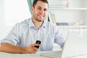 Smiling businessman holding his cell while typing on his laptop