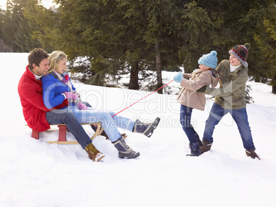 Young Girl And Boy Pulling Parents Through Snow On Sled