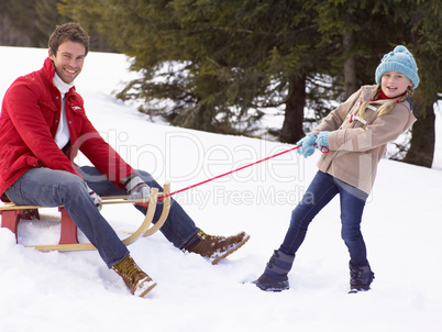 Young Girl Pulling Father Through Snow On Sled