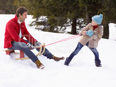 Young Girl Pulling Father Through Snow On Sled