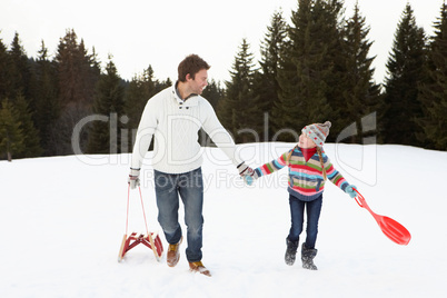 Young Father And Daughter Walking In Snow With Sleds