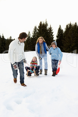 Young Family In Alpine Snow Scene With Sled