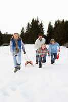 Young Family Running Through Snow With Sled