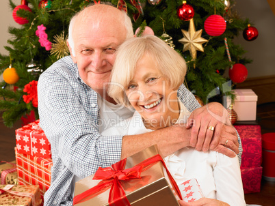Senior couple with gifts in front of Christmas tree