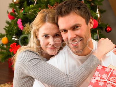 Young couple with gifts in front of Christmas tree