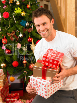 Young man holding gifts in front of Christmas tree