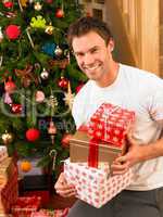 Young man holding gifts in front of Christmas tree