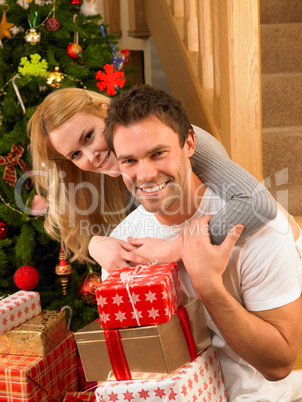 Young couple with gifts in front of Christmas tree