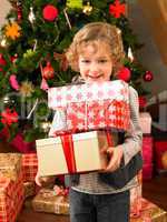Young child holding gifts in front of Christmas tree