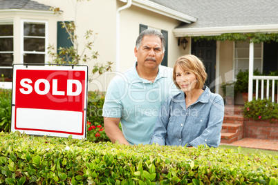 Senior Hispanic couple outside house with sold sign