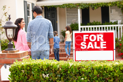 Hispanic family outside home with for sale sign