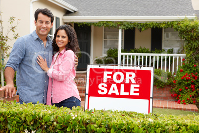 Hispanic couple outside home with for sale sign