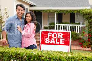 Hispanic couple outside home with for sale sign