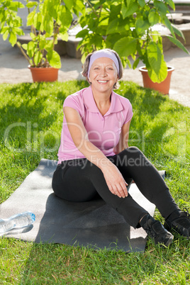 Senior sportive woman sitting on mat sunny