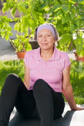 Senior sportive woman sitting on mat sunny