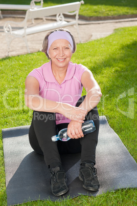 Senior sportive woman sitting on mat sunny