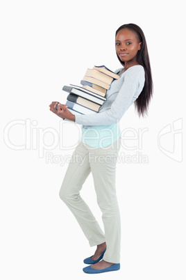 Side view of young woman carrying a stack of books