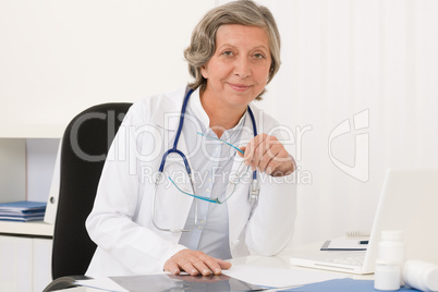 Senior doctor female sit behind office desk