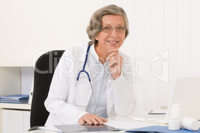 Senior doctor female sit behind office desk