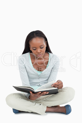 Young woman sitting on the floor turning the page of her book