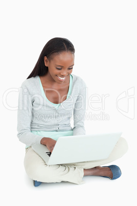 Smiling woman working on her laptop sitting on the floor