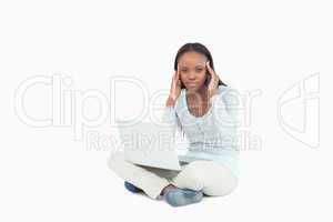 Young woman sitting on the floor with headache over her laptop
