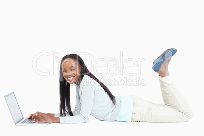 Side view of smiling woman lying on the floor with her laptop