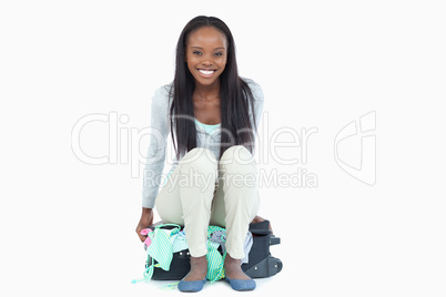 Smiling young woman sitting on her suitcase