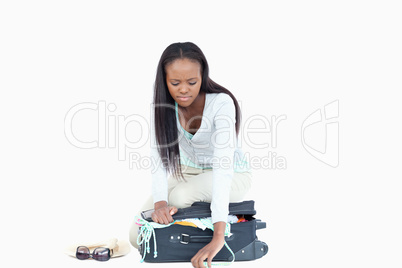 Young woman having problems closing her suitcase