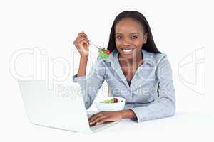 Joyful businesswoman working with a laptop while eating a salad
