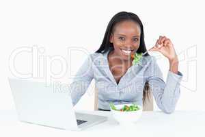 Cute businesswoman working with a notebook while eating a salad