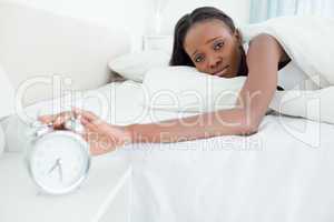 Tired young woman switching off her alarm clock