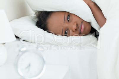 Woman covering her ears while her alarm clock is ringing