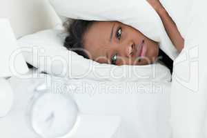 Tired woman covering her ears while her alarm clock is ringing