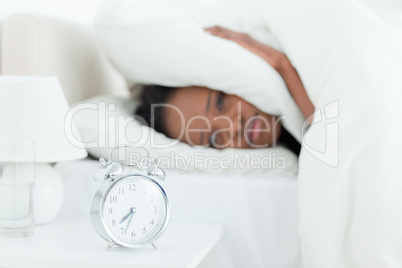 Young woman covering her ears while her alarm clock is ringing