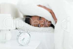 Young woman covering her ears while her alarm clock is ringing