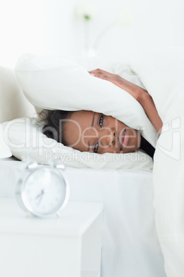 Portrait of a woman covering her ears while her alarm clock is r