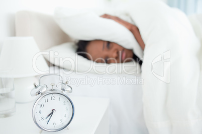 Exhausted woman covering her ears while her alarm clock is ringi