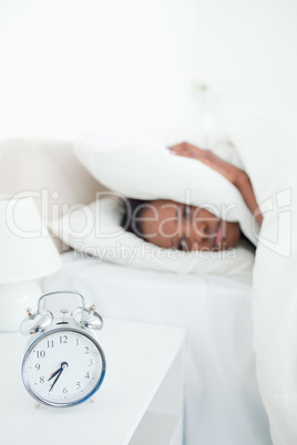 Portrait of a tired woman covering her ears while her alarm cloc