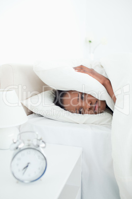 Portrait of a young woman covering her ears while her alarm cloc