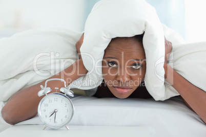 Exhausted woman covering her ears with a duvet