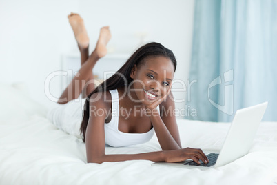 Happy woman lying on her belly using a laptop