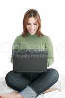 Excited girl in jeans with laptop sitting on her bed isolated