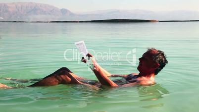 Man reads a relaxed lying in Dead Sea water.