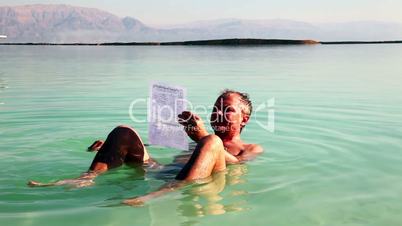Man reads a newspaper while bathing in the Dead Sea.